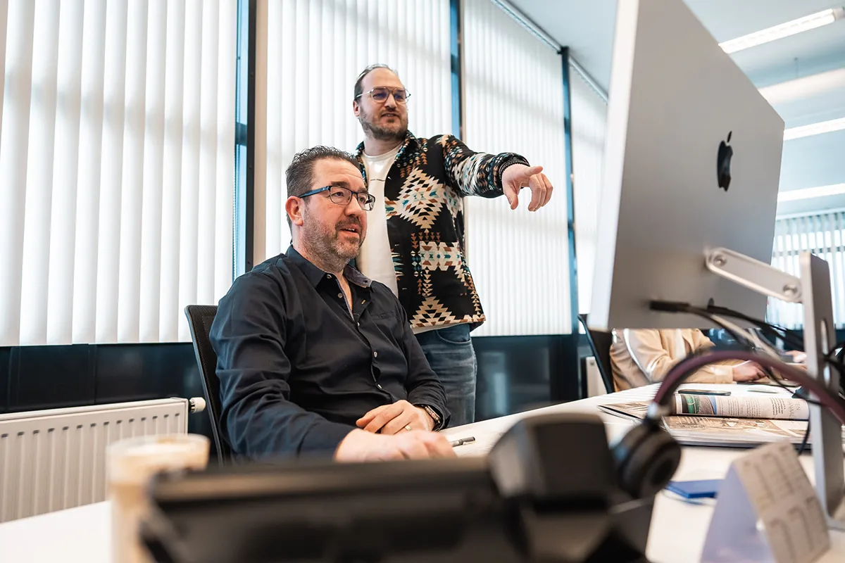 Overleg aan een werkplek met beeldscherm op het kantoor van Louwers Mediagroep